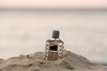 Bottle of luxury perfume on beach sand near ocean