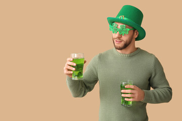 Young man in leprechaun hat with glasses of beer on brown background. St. Patrick's Day celebration