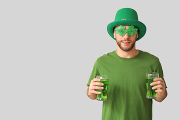Young man in leprechaun hat with glasses of beer on grey background. St. Patrick's Day celebration