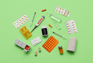 Pulse oximeter, thermometer, bandage and medicines on green background