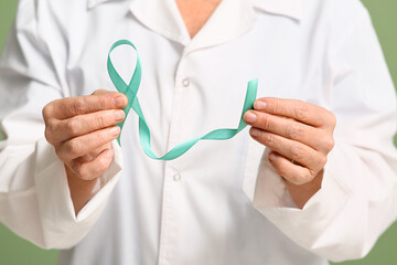 Mature female doctor with teal ribbon on green background, closeup. Cervical Health Awareness Month