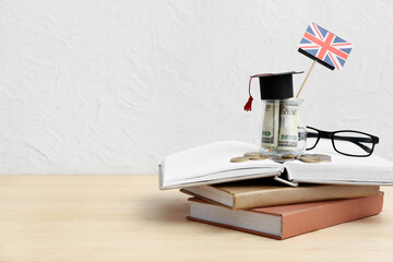 Jar of money with UK flag and books on table near light wall. Student loan concept