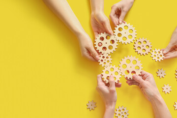 Obraz premium Hands holding wooden gears on yellow background, top view