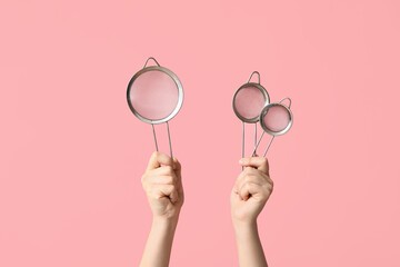 Female hands with sieves on pink background