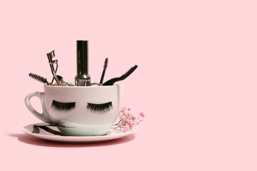 Cup with false eyelashes, mascara and tools on pink background