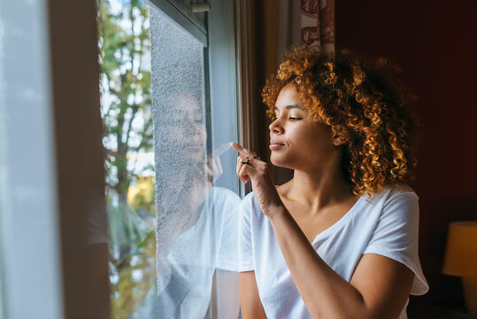 Woman touching window glass while looking out on rainy day