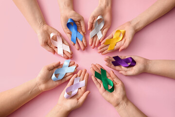 Many female hands with different ribbons on pink background, closeup. World Cancer Day