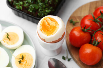 Boiled eggs, tomatoes and microgreens on white tiled table, closeup
