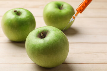 GMO concept. Injecting green apples with syringe at wooden table, closeup