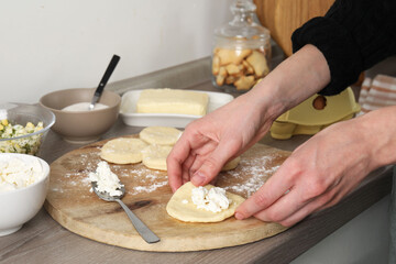 Woman making pirozhki (stuffed pastry pies) with cottage cheese at countertop indoors, closeup