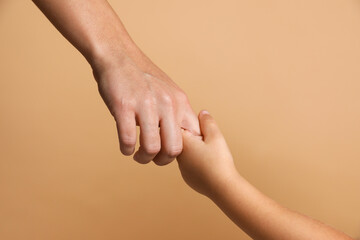 Mother and child holding hands on beige background, closeup