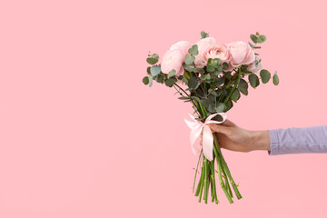 Female hands with bouquet of ranunculus flowers and eucalyptus on pink background