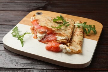 Delicious crepes with salmon, cream cheese and arugula on wooden table, closeup