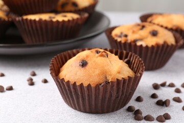 Delicious muffin with chocolate chips on light grey table, closeup
