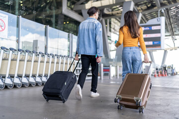 Rear view of young couple walking in airport terminal to boarding gate.