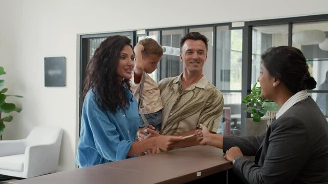 Stab slowmo shot of female Indian receptionist giving key card to Caucasian family of three checking in at hotel reception