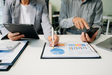 Business documents on office table with smart phone and laptop and two colleagues discussing data