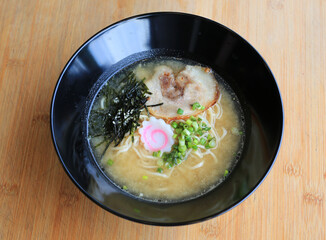 Miso Ramen Asian noodles with chashu Pork, seaweed and boiled egg in black bowl on bamboo wooden background.
