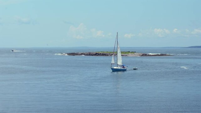 A sailboat sailing into the harbor pulling a small dinghy at Monhegan Island in Maine.