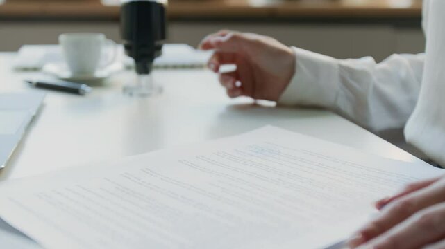 Closeup of hands of anonymous female secretary or paralegal studying agreement, then stamping documents with company seal while working at desk in office
