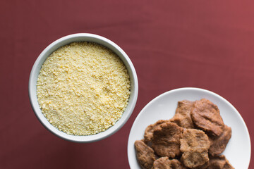 Overhead view of kuli-kuli and yellow garri in a white bowl, top view of nigerian groundnut cakes and garri in a bowl, fresh homemade nigerian kulikuli and cassava in a ceramic bowl