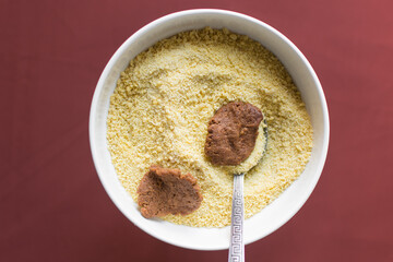 Overhead view of kuli-kuli and yellow garri in a white bowl, top view of nigerian groundnut cakes and garri in a bowl, fresh homemade nigerian kulikuli and cassava in a ceramic bowl