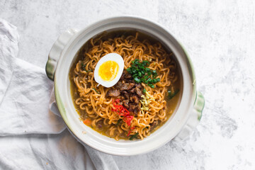 Overhead view of Spicy vegetable instant noodles with broth in a claypot, top view of veggie ramen noodles with soft boiled egg minced pork with broth in a donabe
