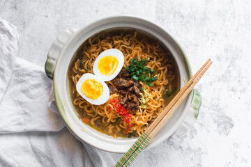 Overhead view of Spicy vegetable instant noodles with broth in a claypot, top view of veggie ramen noodles with soft boiled egg minced pork with broth in a donabe