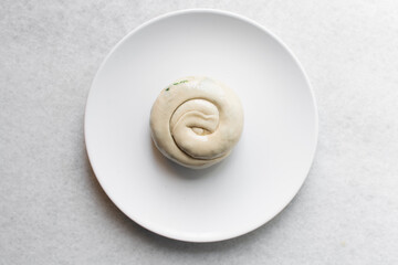 Overhead view of raw chinese scallion pancakes being rolled on white countertop, top view of homemade scallion pancakes, process of making cong you bing