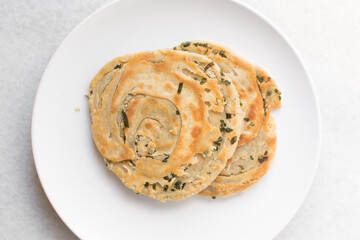 Overhead view of chinese scallion pancakes on a white plate, top view of golden-brown homemade scallion pancakes, process of making cong you bing