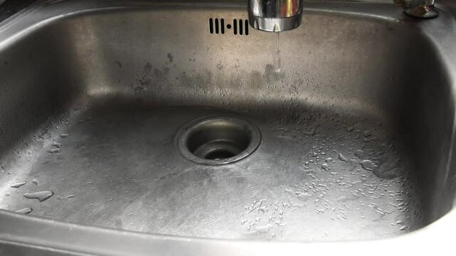 water drop dripping from leak silver chrome faucet into wet aluminum sink