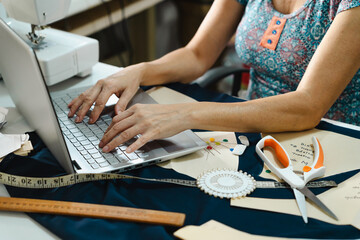 Unrecognizable woman using laptop in a sewing workspace, managing fashion business and industry. Technology in small business concept.