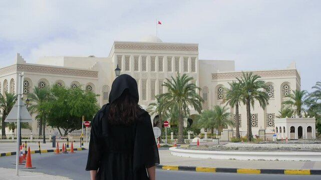Rear view of woman wearing burkha looking at Al Fateh Mosque. Female tourist is standing on roadside during windy day. She is traveling in Manama, Bahrain.