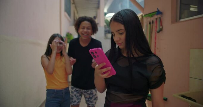 Teenagers mocking friend over unflattering photo reveal on smartphone in suburban alleyway, highlighting social dynamics, peer pressure, and media influence