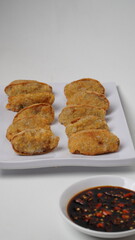 A plate of fried tofu walik served with soy sauce and chili sauce using a separate white plate placed on a white base and background (isolated white).
