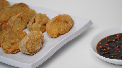 A plate of fried tofu walik served with soy sauce and chili sauce using a separate white plate placed on a white base and background (isolated white).