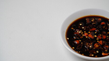 Sweet soy sauce chili sauce with sliced ​​red cayenne pepper served on a white plate placed on a white base and background (isolated white).