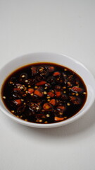 Sweet soy sauce chili sauce with sliced ​​red cayenne pepper served on a white plate placed on a white base and background (isolated white).