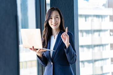 社内でノートパソコンを持ち指差しをする女性