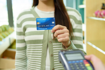 Customers pay with credit cards at fruit shop with small business owners. Close-up of a blue credit card held by a customer before completing a wireless digital transaction.