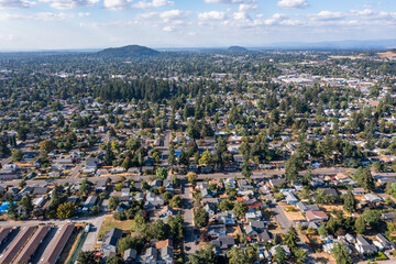 Aerial drone view of Southeast Portland, Oregon, showcasing residential neighborhoods, tree-lined streets, urban landscape, and distant downtown skyline under a partly cloudy sky