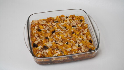 Whole pumpkin bread pudding topped with raisins and sliced ​​almonds served in a glass baking dish placed on a white background (isolated white).