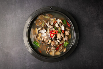 Seafood soup with clams, mussels and chili peppers in bowl on dark background, top view