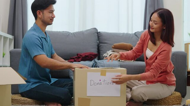 group of asian young adults sorting and packing clothes into donation box. community support, and charitable giving