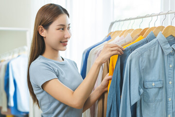 Choose clothes to wear, attractive asian young woman, girl try on appare, happy choice of shirt, female outfit on hanger in wardrobe in room closet at home. Deciding blouse what to put on which one
