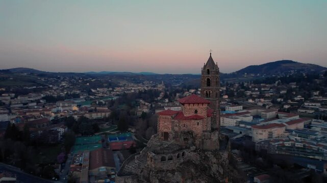 aerial shot around saint michel d'aiguilhe rock and chapel just before sunrise in Le Puy en Velay, Haute Loire department, Auvergne Rhone Alpes region, France