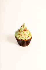 A cupcake with green frosting and colorful sprinkles sits on a white background. The frosting has a swirled texture, and the base is in a brown paper cup