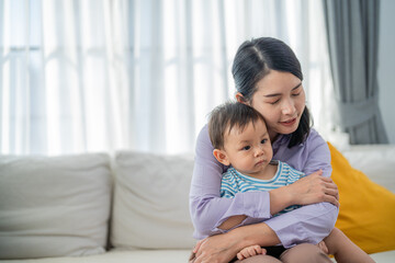 Mother comforting child while sitting on a couch in a bright living room during the morning