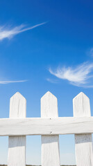white picket fence against clear blue sky with wispy clouds
