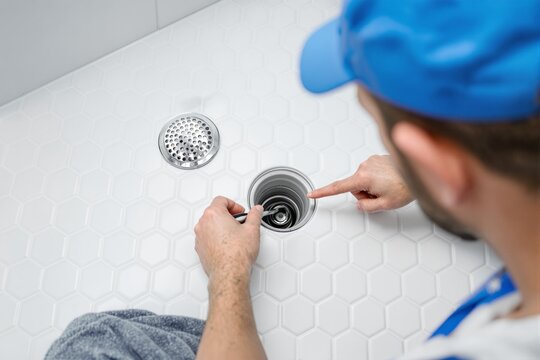 Professional plumber unclogging a shower drain using a specialized tool on a white tiled background. Concept of plumbing maintenance and repair. Ai generative